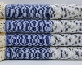 May include: A stack of four blue and white patterned Turkish towels with fringe edges. The towels are folded and stacked on a white surface.