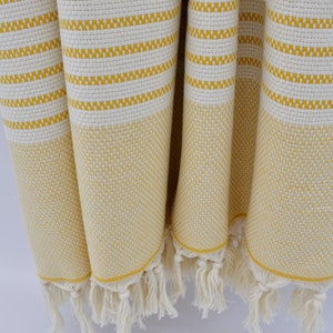 May include: A yellow and white striped Turkish towel with fringe. The towel is made of cotton and is soft and absorbent.