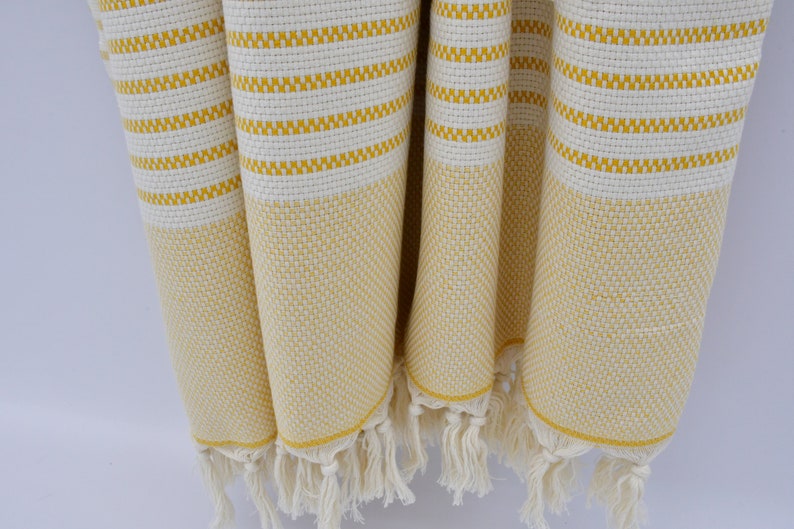 May include: A yellow and white striped Turkish towel with fringe. The towel is made of cotton and is soft and absorbent.