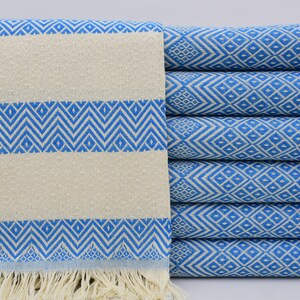 Puede incluir: Una pila de toallas turcas con estampado azul y blanco con flecos. Las toallas están dobladas y apiladas sobre una superficie blanca.