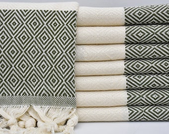 May include: A stack of white Turkish towels with green diamond patterned borders. The towels have fringe on the bottom.