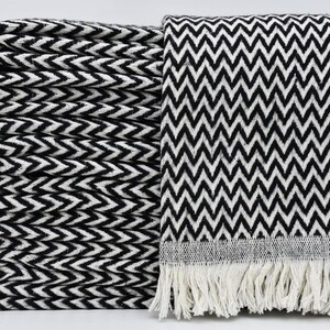 May include: A stack of four black and white chevron patterned throw blankets with fringe on the bottom.