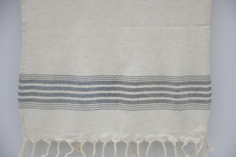 May include: A white cotton kitchen towel with a black striped border and fringe.
