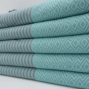 May include: Stack of five turquoise and gray striped towels with fringe edges. The towels have a geometric pattern.