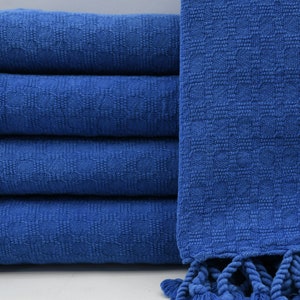 May include: A stack of four blue textured towels with a woven pattern and fringed edges. The towels are a vibrant shade of blue, and the fringe adds a decorative element. The towels are neatly folded.