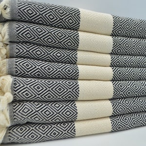 May include: A stack of black and white patterned Turkish towels with fringe edges. The towels are folded and arranged in a neat pile.
