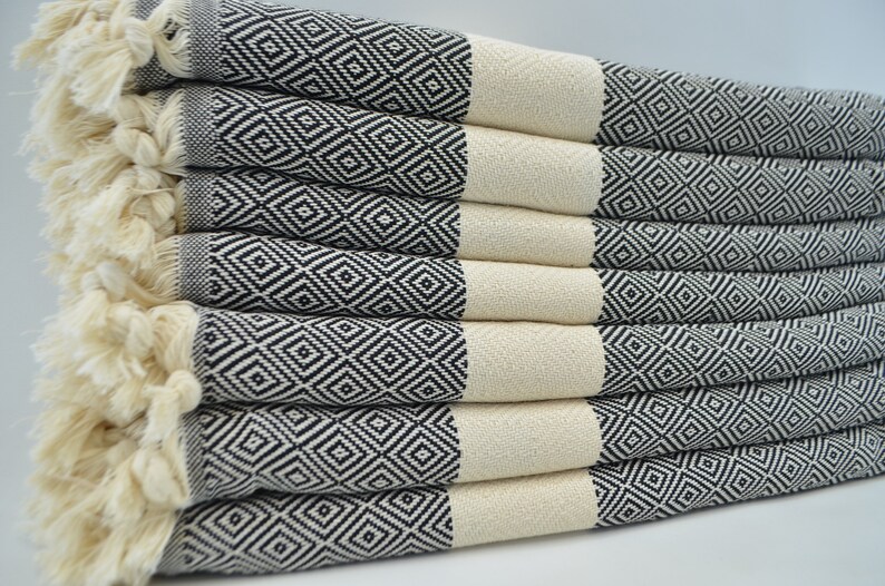 May include: A stack of black and white patterned Turkish towels with fringe edges. The towels are folded and arranged in a neat pile.