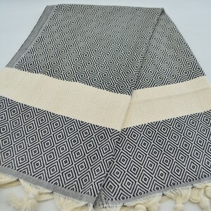 May include: A black and white patterned Turkish towel with a cream colored stripe and fringe. The towel is folded in half and has a diamond pattern.