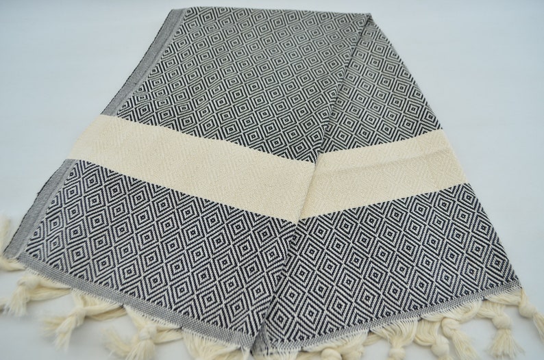 May include: A black and white patterned Turkish towel with a cream colored stripe and fringe. The towel is folded in half and has a diamond pattern.