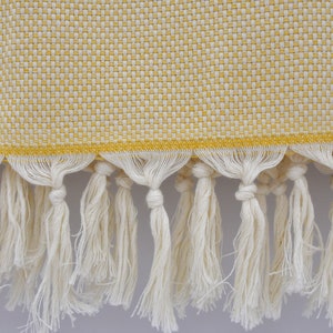 May include: A yellow and white woven throw blanket with a fringe border. The fringe is made of white cotton.