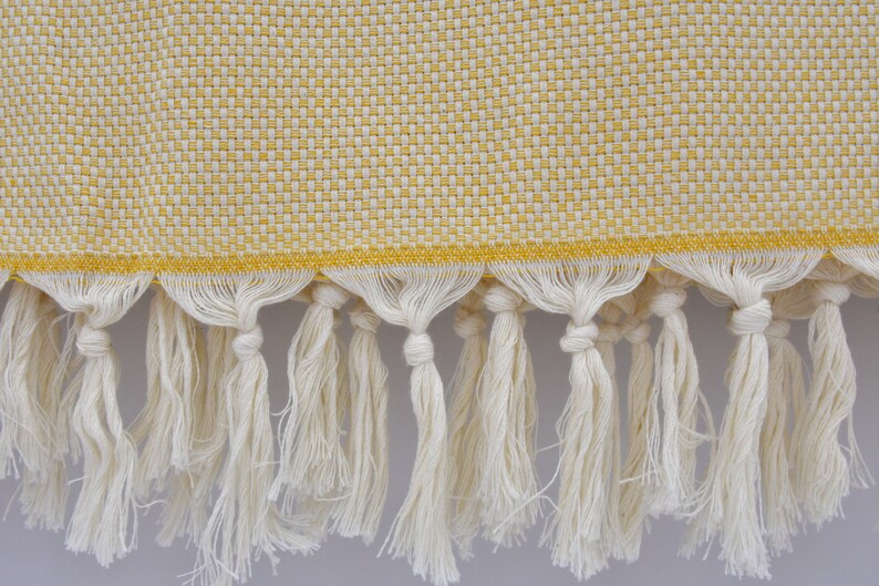 May include: A yellow and white woven throw blanket with a fringe border. The fringe is made of white cotton.
