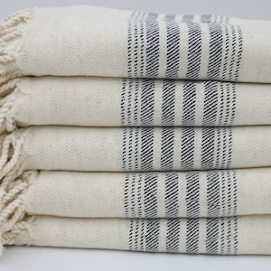 May include: A stack of five white towels with blue stripes and fringe edges.