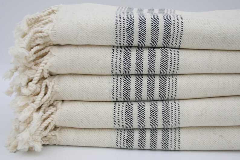 May include: A stack of five white towels with blue stripes and fringe edges.