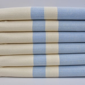 May include: A stack of six towels with a white background and light blue stripes. The towels have a fringe on the edges.