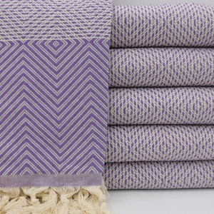 May include: A stack of purple and white patterned Turkish towels with fringe. The towels are folded and stacked on a white surface.