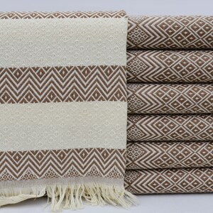 Puede incluir: Una pila de toallas rayadas de color marrón y blanco con flecos. Las toallas tienen un patrón geométrico.