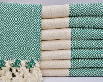May include: A stack of green and white patterned Turkish towels with fringe. The towels are folded and stacked on a white surface.
