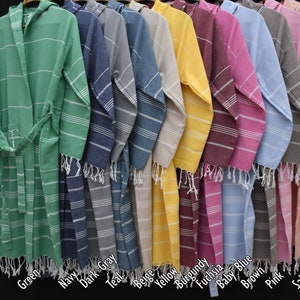May include: A row of ten hooded Turkish towels in various colors, including green, navy, dark gray, teal, beige, yellow, burgundy, fuchsia, baby blue, brown, pink, and salmon. The towels are lined up in a row, with the hoods facing the viewer. The towels are all made of a soft, absorbent cotton.