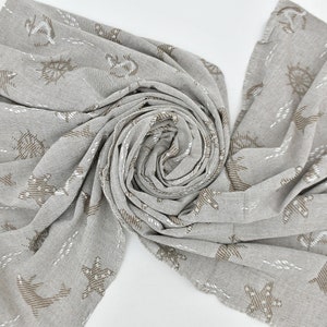 May include: A grey and brown woven throw blanket with a nautical theme. The blanket features a repeating pattern of anchors, stars, and fish.