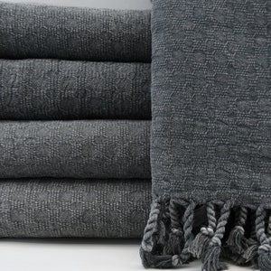 May include: A stack of four gray Turkish towels with fringed edges. The towels are made of a soft, absorbent cotton.