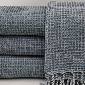 May include: A stack of four blue waffle weave towels with fringe edges. The towels are folded and stacked on a white surface.