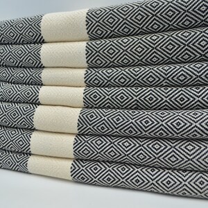 May include: A stack of white and black patterned Turkish towels. The towels are folded and arranged in a neat pile. The towels have a diamond pattern.