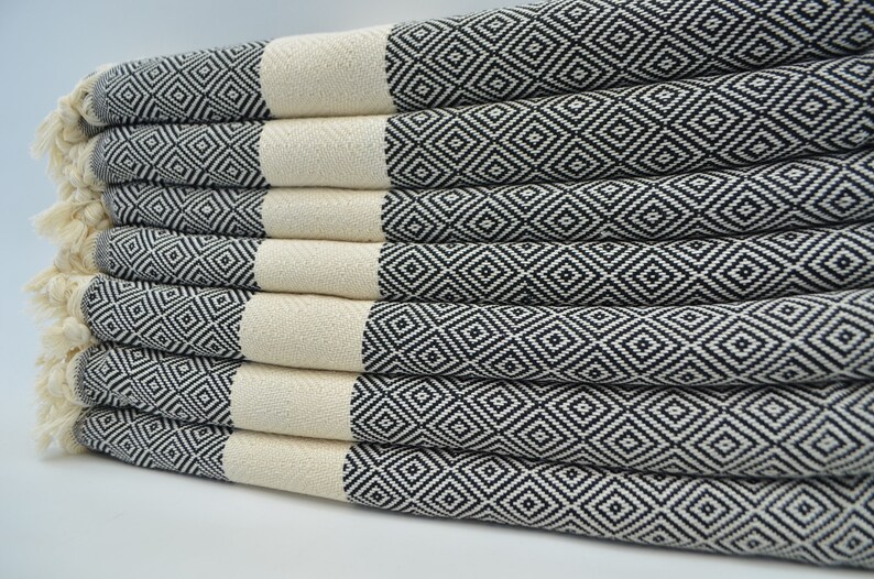 May include: A stack of white and black patterned Turkish towels. The towels are folded and arranged in a neat pile. The towels have a diamond pattern.