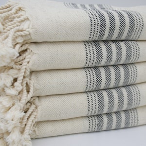 May include: A stack of white towels with black stripes and fringe. The towels are folded neatly and have a soft, textured appearance.