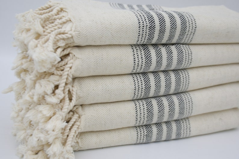 May include: A stack of white towels with black stripes and fringe. The towels are folded neatly and have a soft, textured appearance.