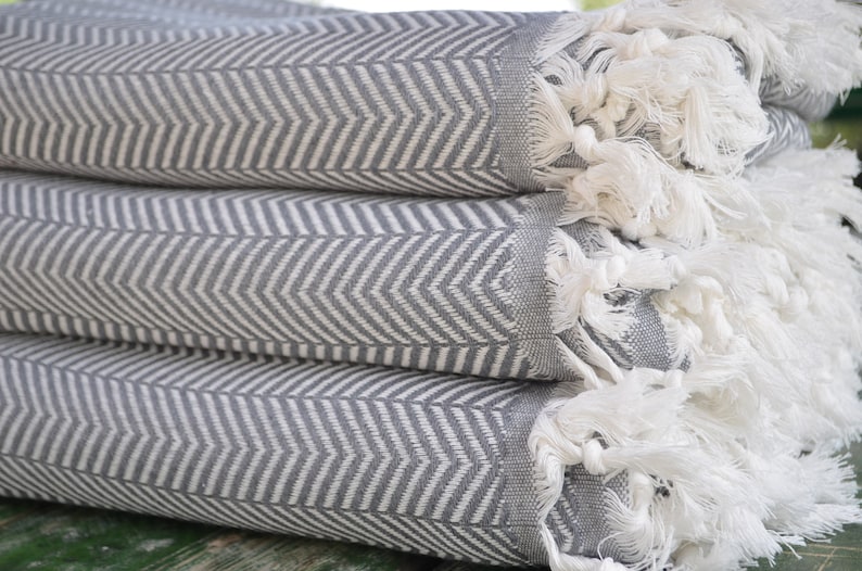 May include: A stack of gray and white striped towels with white fringe. The towels are folded and stacked on top of each other.
