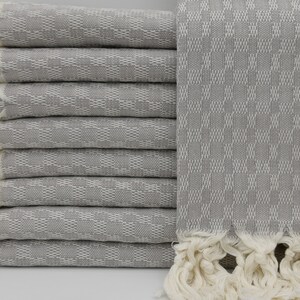 May include: A stack of gray Turkish towels with white fringe. The towels have a woven pattern and are folded neatly.