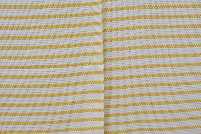 May include: White fabric with yellow stripes. The fabric has a woven texture.