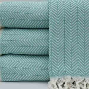 May include: A stack of four turquoise and white patterned towels with white fringe. The towels are folded and stacked on a white surface.