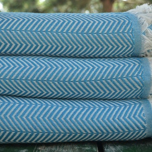 May include: Three blue and white striped towels with white fringe are stacked on top of each other. The towels have a herringbone pattern.
