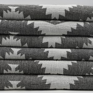 May include: A stack of six grey and white patterned towels with fringed edges.