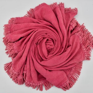 Könnte beinhalten: Eine rosa Wolldecke mit Fransen ist zu einer Spirale zusammengerollt.