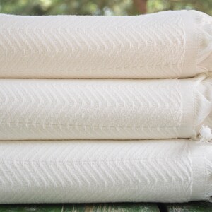 May include: A stack of three white cotton towels with a herringbone pattern and fringe edges.
