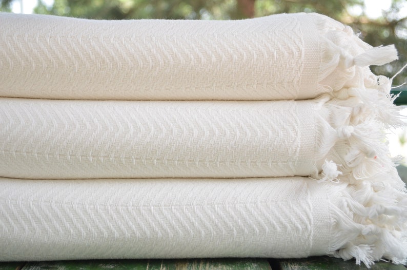 May include: A stack of three white cotton towels with a herringbone pattern and fringe edges.