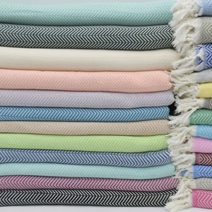 May include: A stack of 20 colorful woven cotton throws with a herringbone pattern. The throws are folded and stacked in a variety of colors, including pink, blue, green, and white.
