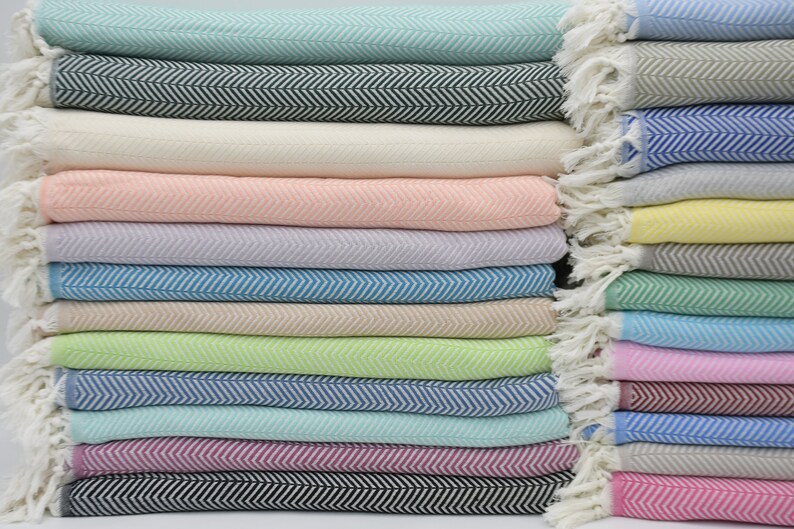 May include: A stack of 20 colorful woven cotton throws with a herringbone pattern. The throws are folded and stacked in a variety of colors, including pink, blue, green, and white.