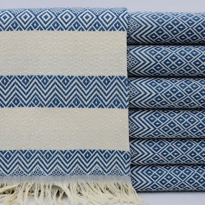 Puede incluir: Una pila de toallas turcas con estampado azul y blanco con flecos. Las toallas están dobladas y apiladas sobre una superficie blanca.