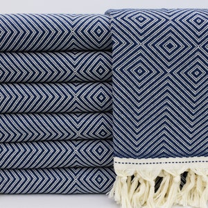 May include: A stack of six navy blue and white patterned towels with fringe. The towels are folded and stacked on a white surface.