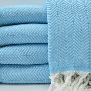May include: A stack of light blue towels with a white chevron pattern and white fringe.