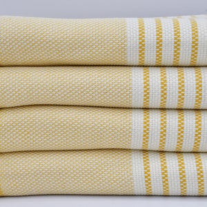 May include: A stack of four yellow and white striped towels with fringed edges. The towels are folded and stacked on a white surface.