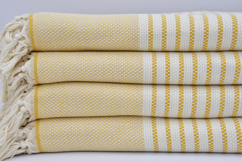 May include: A stack of four yellow and white striped towels with fringed edges. The towels are folded and stacked on a white surface.