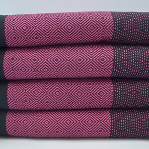May include: Four black and pink patterned towels stacked on top of each other. The towels have a diamond pattern with black and pink stripes on the edges.
