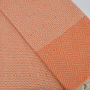 May include: Orange and white patterned Turkish towel with fringe. The towel has a geometric design.