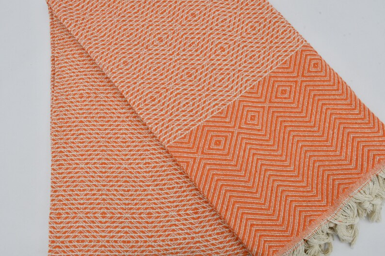 May include: Orange and white patterned Turkish towel with fringe. The towel has a geometric design.