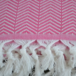 May include: Pink and white patterned towel with white fringe. The towel has a chevron pattern.