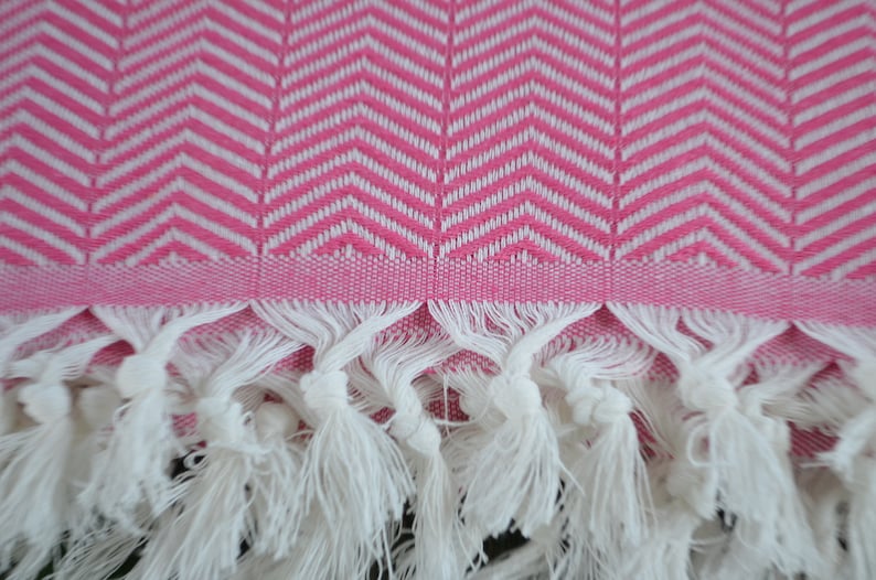 May include: Pink and white patterned towel with white fringe. The towel has a chevron pattern.